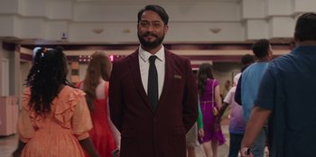 Movie still from “13: The Musical” (2022), directed by Tamra Davis – A man in a suit and tie standing in front of a group of people; Medium shot, Over the shoulder angle