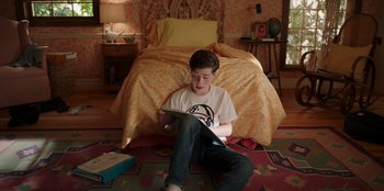 Movie still from “13: The Musical” (2022), directed by Tamra Davis – A young man sitting on the floor in front of a bed; Medium shot, High angle