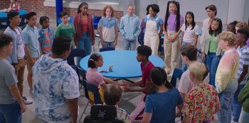 Movie still from “13: The Musical” (2022), directed by Tamra Davis – A group of people sitting around a table; Wide shot, Over the shoulder angle