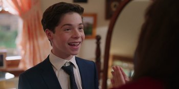 Movie still from “13: The Musical” (2022), directed by Tamra Davis – A young man wearing a suit and tie smiling; Close Up shot, Over the shoulder angle
