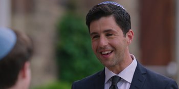 Movie still from “13: The Musical” (2022), directed by Tamra Davis – A man in a suit and tie smiling for the camera; Close Up shot, Over the shoulder angle