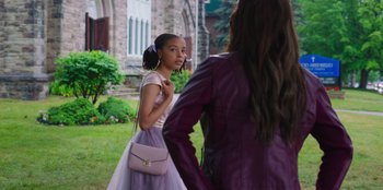 Movie still from “13: The Musical” (2022), directed by Tamra Davis – A young girl in a purple dress is talking to an older woman in a purple jacket; Medium shot, Over the shoulder angle
