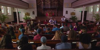 Movie still from “13: The Musical” (2022), directed by Tamra Davis – A group of people sitting in a church; Extreme Wide shot, High angle