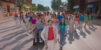 Movie still from “13: The Musical” (2022), directed by Tamra Davis – A large group of people walking down a street; Wide shot, High angle