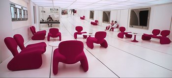 Movie still from “2001: A Space Odyssey” (1968), directed by Stanley Kubrick – A group of red chairs in a room with white walls; Wide shot, High angle