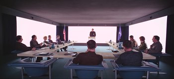Movie still from “2001: A Space Odyssey” (1968), directed by Stanley Kubrick – A group of people sitting in a room with a man standing at a podium in front; Wide shot, Over the shoulder angle