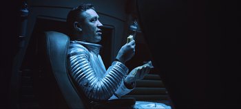 Movie still from “2001: A Space Odyssey” (1968), directed by Stanley Kubrick – A man sitting in a chair holding a piece of food; Medium shot, Low angle