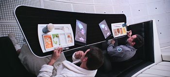 Movie still from “2001: A Space Odyssey” (1968), directed by Stanley Kubrick – A man sitting in front of a tv eating food; Medium shot, Overhead angle