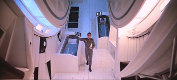 Movie still from “2001: A Space Odyssey” (1968), directed by Stanley Kubrick – A man standing in a room holding a cell phone; Wide shot, Overhead angle
