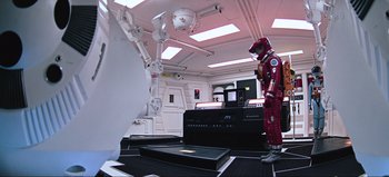 Movie still from “2001: A Space Odyssey” (1968), directed by Stanley Kubrick – A red suit is on a table next to a laptop; Wide shot, High angle