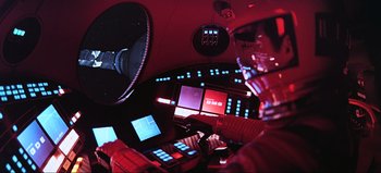 Movie still from “2001: A Space Odyssey” (1968), directed by Stanley Kubrick – A person is sitting at a desk in a room; Medium shot, Low angle
