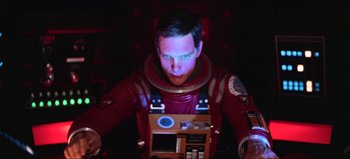 Movie still from “2001: A Space Odyssey” (1968), directed by Stanley Kubrick – A man in a space suit is sitting at a desk; Medium shot, Overhead angle