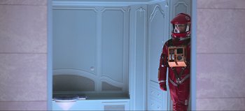 Movie still from “2001: A Space Odyssey” (1968), directed by Stanley Kubrick – A man in a red suit is holding a box; Wide shot, Overhead angle