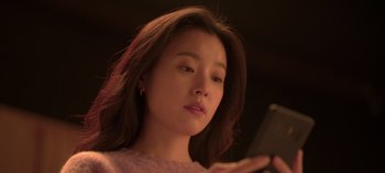 Movie still from “20th Century Girl” (2022), directed by Woo-ri Bang – A woman looking at her cell phone in a dimly - lit room; Close Up shot, Low angle