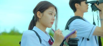 Movie still from “20th Century Girl” (2022), directed by Woo-ri Bang – A young woman writing on a piece of paper while standing outside; Close Up shot, Over the shoulder angle