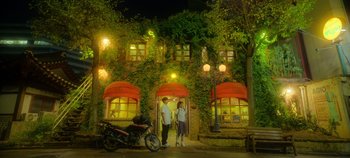Movie still from “20th Century Girl” (2022), directed by Woo-ri Bang – A man and a woman standing in front of a building at night; Extreme Wide shot, Low angle