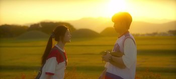 Movie still from “20th Century Girl” (2022), directed by Woo-ri Bang – A couple of people that are standing in the grass; Wide shot, Low angle