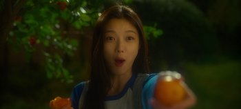 Movie still from “20th Century Girl” (2022), directed by Woo-ri Bang – A young woman holding an orange in her hand; Close Up shot, Over the shoulder angle