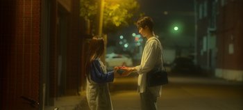 Movie still from “20th Century Girl” (2022), directed by Woo-ri Bang – A man and a woman are exchanging a gift; Medium shot, Over the shoulder angle