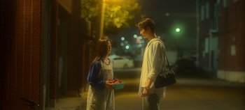 Movie still from “20th Century Girl” (2022), directed by Woo-ri Bang – A young man and a young woman standing on a sidewalk; Medium shot, Over the shoulder angle