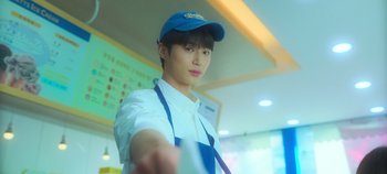 Movie still from “20th Century Girl” (2022), directed by Woo-ri Bang – A man in a blue hat and apron is holding something; Close Up shot, Low angle