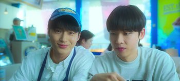 Movie still from “20th Century Girl” (2022), directed by Woo-ri Bang – Two young men sitting next to each other at a table; Close Up shot, Over the shoulder angle