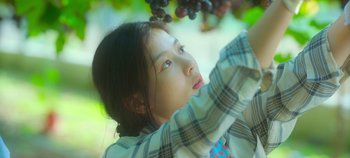 Movie still from “20th Century Girl” (2022), directed by Woo-ri Bang – A young girl holding onto a bunch of grapes; Close Up shot, Low angle