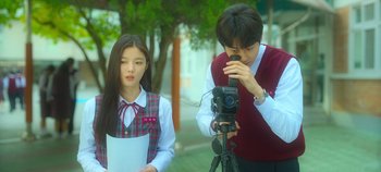 Movie still from “20th Century Girl” (2022), directed by Woo-ri Bang – A man and a woman standing next to a camera; Medium shot, Low angle