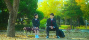 Movie still from “20th Century Girl” (2022), directed by Woo-ri Bang – Two young people sitting on a bench in a park; Wide shot, Over the shoulder angle