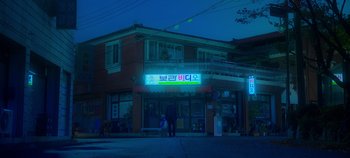 Movie still from “20th Century Girl” (2022), directed by Woo-ri Bang – A person standing outside of a store at night; Extreme Wide shot, Low angle