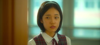 Movie still from “20th Century Girl” (2022), directed by Woo-ri Bang – A young girl in a school uniform is looking at the camera; Close Up shot, High angle