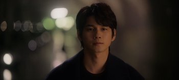 Movie still from “20th Century Girl” (2022), directed by Woo-ri Bang – A young man with long black hair is looking at the camera; Close Up shot, Over the shoulder angle