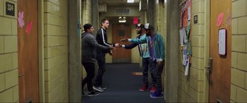 Movie still from “22 Jump Street” (2014), directed by Phil Lord – A group of young men standing around each other in a hallway; Wide shot, Overhead angle