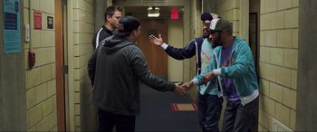 Movie still from “22 Jump Street” (2014), directed by Phil Lord – A group of people standing around each other in a hallway; Medium shot, Over the shoulder angle