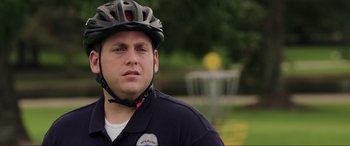 Movie still from “22 Jump Street” (2014), directed by Phil Lord – A police officer wearing a bicycle helmet in front of a fountain; Close Up shot, Over the shoulder angle