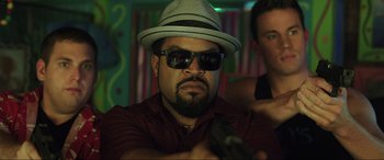 Movie still from “22 Jump Street” (2014), directed by Phil Lord – A man wearing a hat and sunglasses is holding a gun; Close Up shot, Over the shoulder angle