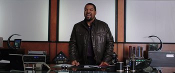 Movie still from “22 Jump Street” (2014), directed by Phil Lord – A man wearing a leather jacket standing in front of a desk; Medium shot, Over the shoulder angle