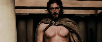 Movie still from “300” (2006), directed by Zack Snyder – A man with a scar on his chest wearing a cape; Medium shot, Low angle