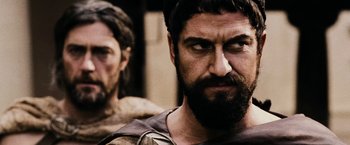 Movie still from “300” (2006), directed by Zack Snyder – A man with a beard is looking at the camera while another man with a beard is looking at the camera; Close Up shot, Over the shoulder angle