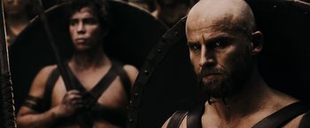 Movie still from “300” (2006), directed by Zack Snyder – A man with a bald head and a long beard; Close Up shot, Over the shoulder angle