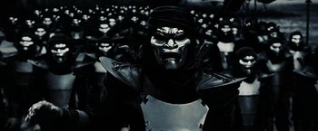 Movie still from “300” (2006), directed by Zack Snyder – A man in a mask and a black hat; Medium shot, High angle