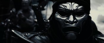 Movie still from “300” (2006), directed by Zack Snyder – A person wearing a mask and holding a sword; Close Up shot, Low angle