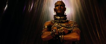 Movie still from “300” (2006), directed by Zack Snyder – A man in chains and gold jewelry is posing for a picture; Close Up shot, Low angle