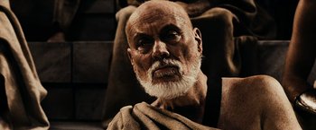 Movie still from “300” (2006), directed by Zack Snyder – An old man with a beard is sitting in a chair; Close Up shot, Low angle