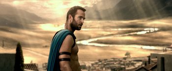 Movie still from “300: Rise of an Empire” (2014), directed by Noam Murro – A man with a beard and a blue shirt is standing in front of a city; Close Up shot, Over the shoulder angle