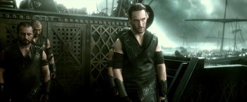 Movie still from “300: Rise of an Empire” (2014), directed by Noam Murro – A man in a leather vest standing in front of a ship; Medium shot, High angle
