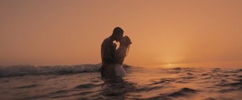 Movie still from “365 Days: This Day” (2022), directed by Tomasz Mandes – A man and a woman kissing in the ocean at sunset; Wide shot, Low angle