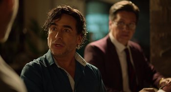 Movie still from “40 Years Young” (2022), directed by Pietro Loprieno – A man with a goatee is looking at the camera while another man in a suit looks on; Close Up shot, Over the shoulder angle