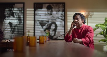 Movie still from “40 Years Young” (2022), directed by Pietro Loprieno – A man sitting at a table talking on the phone; Medium shot, Low angle