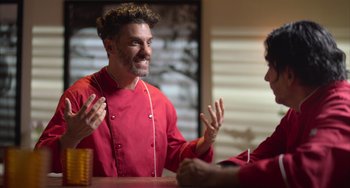 Movie still from “40 Years Young” (2022), directed by Pietro Loprieno – Two people talking to each other in a kitchen; Medium shot, Over the shoulder angle